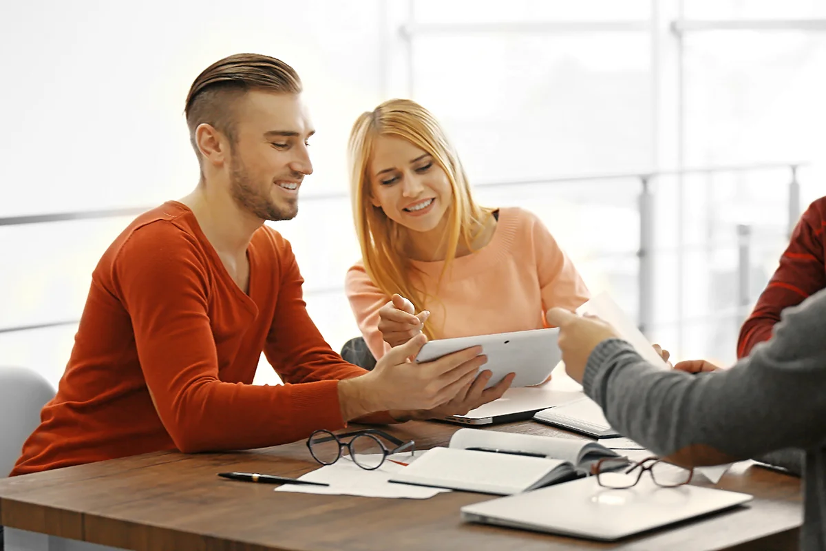 Drei Personen sitzen an einem Tisch und betrachten gemeinsam ein Tablet