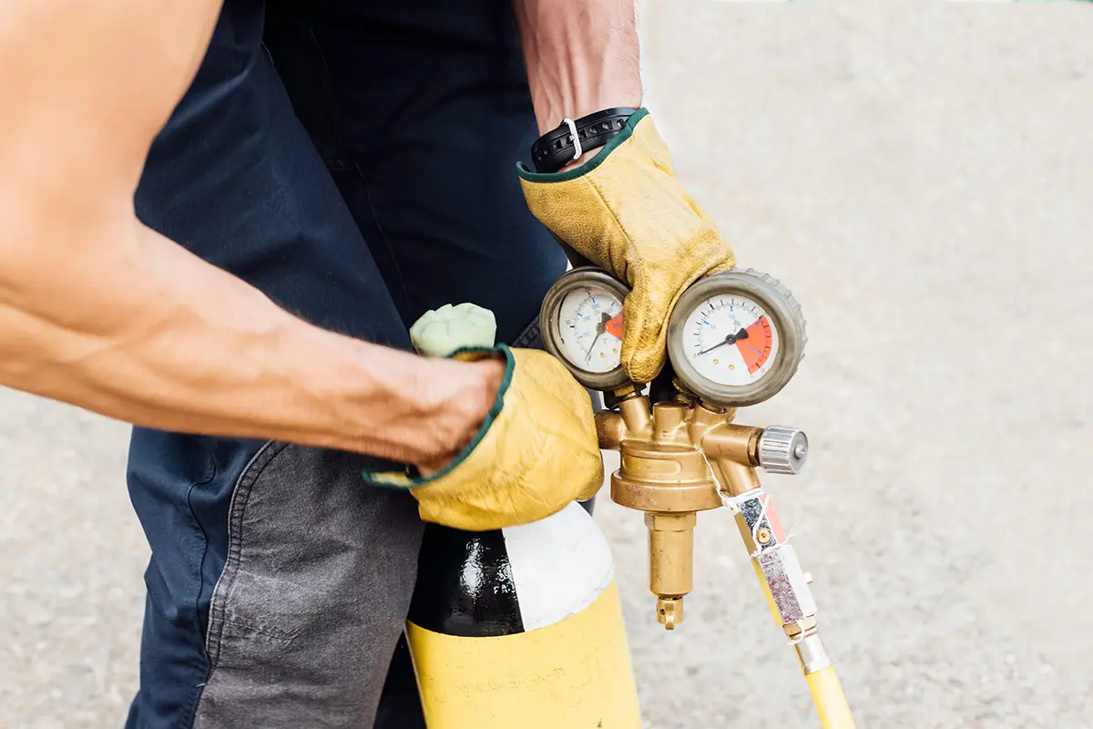 Ein Mann trägt gelbe Handschuhe und hält einen Gasbehälter