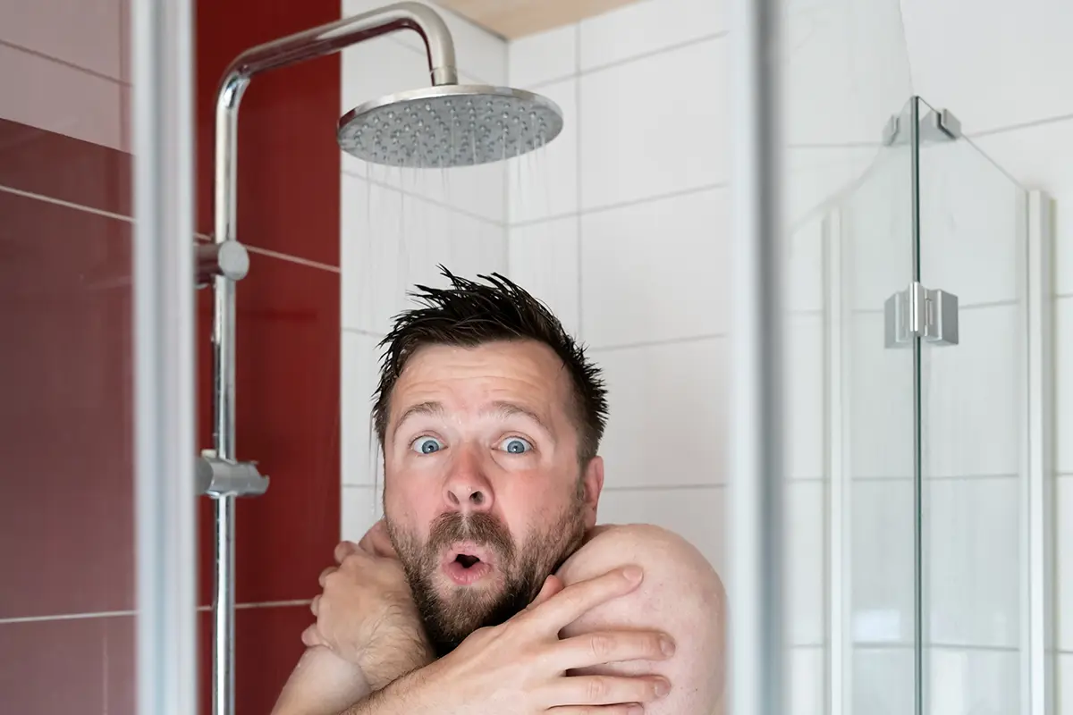 Ein Mann steht unter der Dusche und zittert vor Kälte