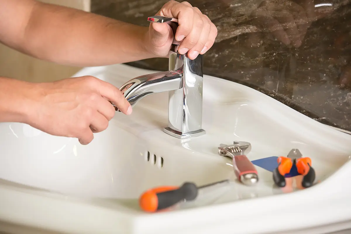 Person repariert Wasserhahn mit Werkzeugen