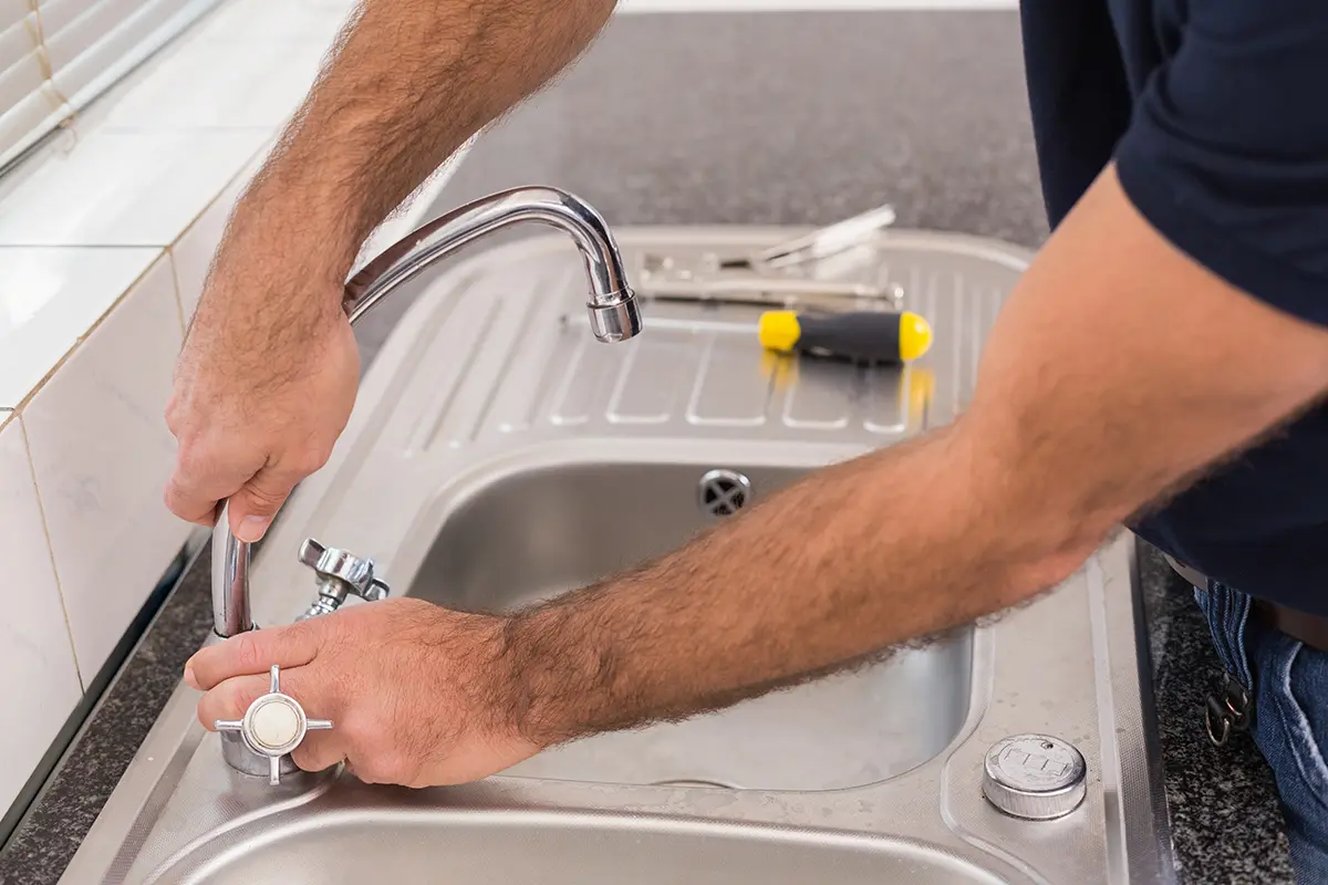 Mann repariert Wasserhahn in der Küche